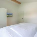 Schlafzimmer mit weißem Bett, Kleiderschrank und Wandbild.