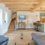 Wohnbereich mit Küchenzeile, Treppenhaus und TV. Holzboden und Deckenbalken.