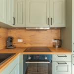 Küche mit Holzoberfläche, grünen Schränken und Edelstahlgeräten.