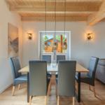 Esszimmer mit Tisch, Stühlen und Sofa. Holzdecke und große Fenster.