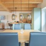 Essbereich mit Holztisch und blauen Stühlen unter Holzbalkendecke.