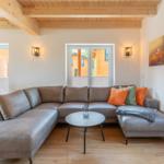 Wohnzimmer mit grauem Sofa, Holzdecke und Blick auf Balkon.