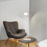 Ein Raum mit grauer Sessel, Beistelltisch und Stehlampe an weißer Wand.