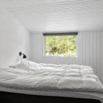 Schlafzimmer mit großem Bett, Fenster mit Waldblick und Wandlampen.