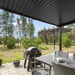 Terrasse mit Tisch, Stühlen, Sonnenschirm und Grill. Blick in den Wald.