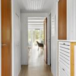 Flur mit weißen Wänden und Holztüren führt zu einem hellen Raum mit Fenster.