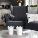 Ein grauer Sessel mit Kissen und Decke vor einem Fenster.