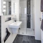 Badezimmer mit Dusche, Waschbecken und beleuchtetem Spiegel.