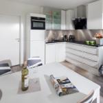 Moderne Küche mit Essbereich und Sitzgelegenheit. Weiße Schränke, schwarze Arbeitsplatten.