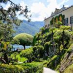 House with garden by lake, surrounded by trees and shrubs.