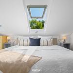 Schlafzimmer mit Dachschrägen, Doppelfenster und Bett mit Kissen.