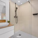 Moderne Dusche mit Glaswand und Waschbecken mit Holzoberfläche.