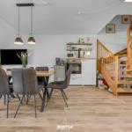 Essbereich mit Tisch, Stühlen und Küchenzeile. Holztreppe führt nach oben.