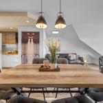 Essbereich mit Holztisch und dunklen Sitzgelegenheiten. Küche und Wohnzimmer sind sichtbar.