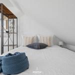 Schlafzimmer mit Bett, Kissen und blauer Decke. Wandregal mit Bildern und Kompass.