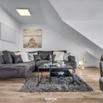 Wohnzimmer mit grauem Sofa, Couchtisch und Wandbild unter Dachschräge.