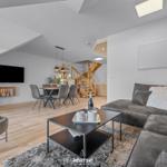 Wohn- und Essbereich mit Sofa, Couchtisch und Fernseher unter schrägen Dachdecken.