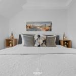 Schlafzimmer mit Dachschrägen, Bett mit Kissen und Wandbild am Kopfende.