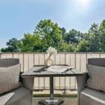 Terrasse mit zwei Stühlen, Tisch und Blumen. Blick auf grüne Bäume.