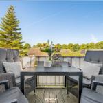 Terrasse mit zwei Sesseln, Tisch und Blumenarrangement. Blick auf Bäume und Häuser.