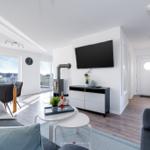 Wohnbereich mit Sofa, TV, Esstisch und Blick auf Balkon.