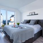 Schlafzimmer mit Blick auf Wasser und Balkon. Bett, Nachttisch und Sessel sind eingerichtet.