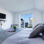 Schlafzimmer mit Blick aufs Wasser und Balkon. Bett, TV und kleiner Tisch.