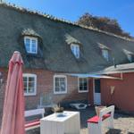 Haus mit Strohdach, Terrasse mit Tisch und Stühlen, Sonnenschirm und Garten.