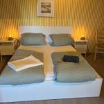 Schlafzimmer mit Bett, Nachttischen und Stühlen. Gelb-weiße Tapete und Wandbild.