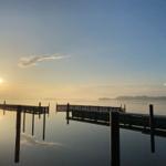 Sonnenuntergang über ruhigem Wasser mit Holzsteg im Vordergrund.
