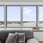 Sofa mit Kissen vor großem Fenster mit Blick auf Wasser und Stadt