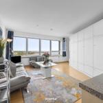 Wohnbereich mit großem Fenster, Sofa, Couchtisch und weißen Schränken.