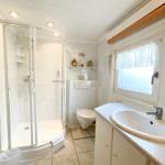 Badezimmer mit Dusche, Waschbecken und Toilette. Fenster mit Vorhang.