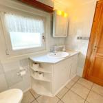 Badezimmer mit Waschbecken, Spiegel, Toilette und Fenster mit Vorhang.