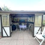 Terrasse mit Pavillon, Tisch, Stühlen und Steinwand. Weiße Gartenstühle und Tisch sind ebenfalls vorhanden.