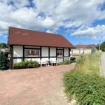 Haus mit Terrasse, Garten und rotem Ziegeldach unter blauem Himmel.