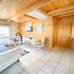 Wohnküche mit Holzwand, Sofa, Esstisch und Küchenzeile.