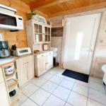 Küche mit Mikrowelle, Kaffeemaschine und Küchenzeile. Tür und Sofa sind sichtbar.