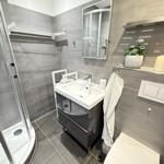 Bad mit Dusche, Waschbecken und Toilette. Graue Fliesen und Spiegelschrank.