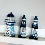 Drei dekorative Leuchttürme mit Seesternen und Ankern auf einem Regal.