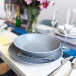 Tisch gedeckt mit grauen Tellern, Blumenvase und Gläsern.