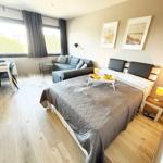 Schlafzimmer mit Bett, Sofa und Tisch. Fenster mit Vorhängen. Wandbilder.