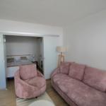 Wohnzimmer mit rosa Sofa und Sessel. Durchgehendes Schlafzimmer mit Bett sichtbar.