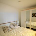 Schlafzimmer mit Doppelbett, Kleiderschrank mit Spiegeltüren und Nachttisch mit Lampe.