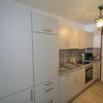 Küche mit hellen Schränken, Spüle und Herd. Holzfußboden und Deckenleuchte.