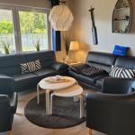 Wohnzimmer mit zwei schwarzen Sofas, runden Tischen und Fensterblick.