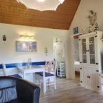 Wohnzimmer mit Esstisch, TV und Küchenzeile. Holzdecke und weiße Möbel.