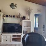 Wohnzimmer mit Fernseher, Schrank und Sessel. Tür führt auf Balkon.