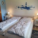 Schlafzimmer mit Doppelbett, zwei Nachttischen und Wandbild mit Leuchtturm.