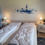 Zwei Betten mit weißen Bettwäsche, Wanddekoration mit Leuchtturm, Nachttische mit Lampen.